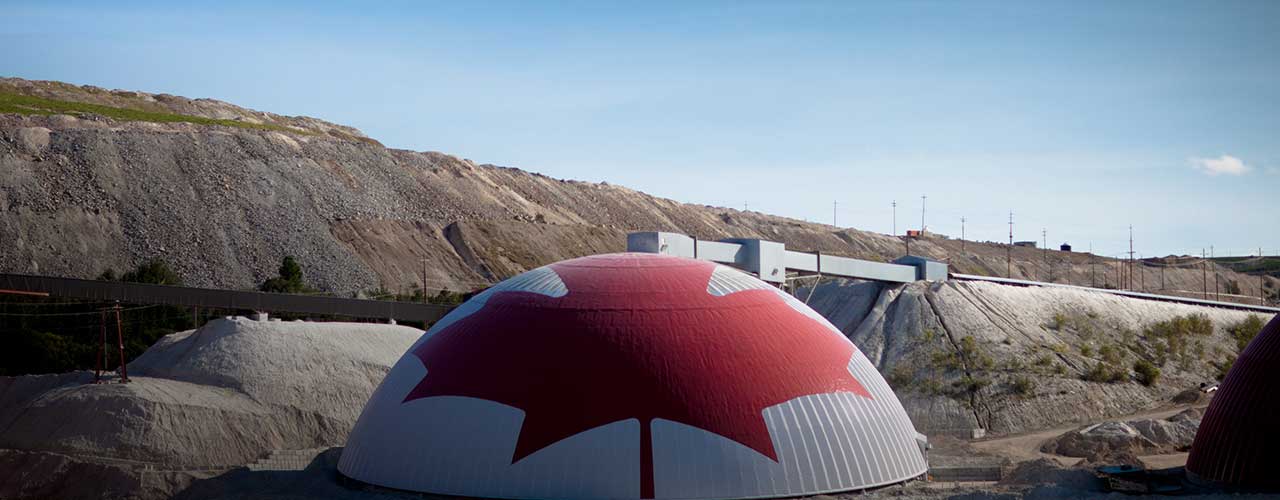 Canadian landscape featuring a large dome with a Canadian flag design, industrial site in the background.